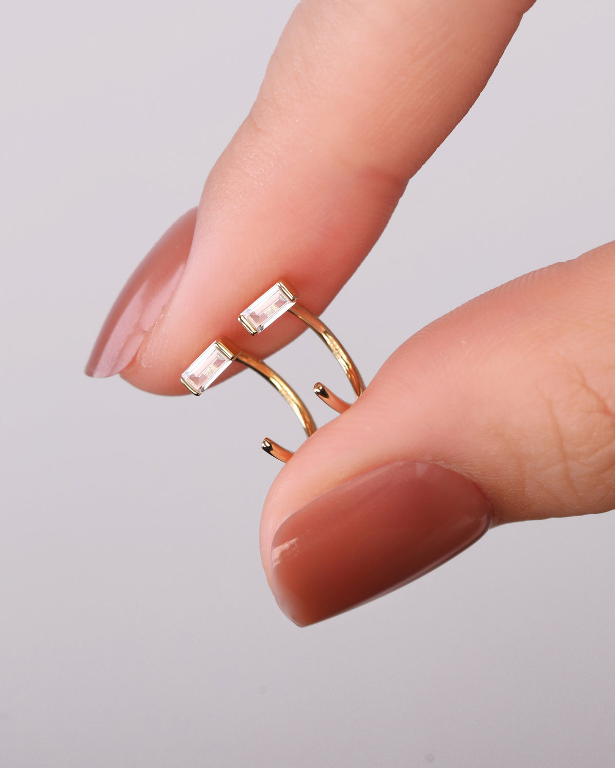 Close-up of gold-tone Meissa Baguette Sparkle Huggie Hoop Earrings with clear baguette-cut stones held between fingers.