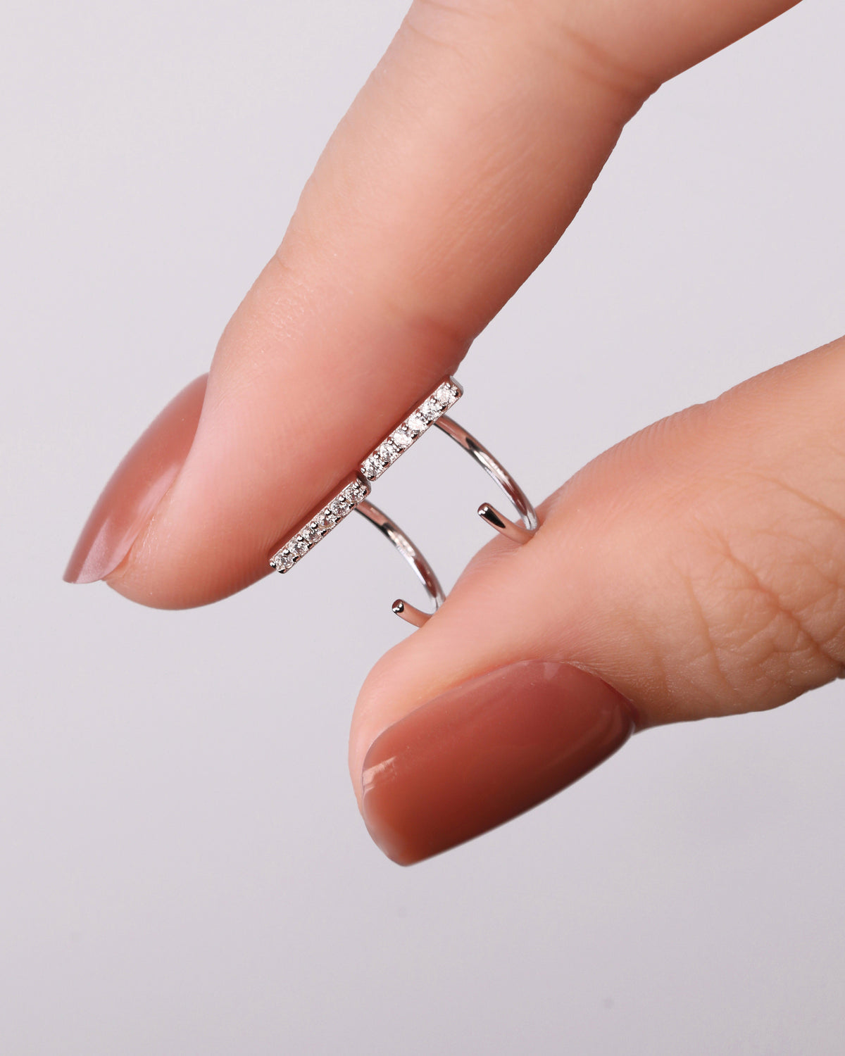 Close-up of silver-tone Meissa Sparkling Bar Huggie Hoop Earrings with clear stones held between fingers.