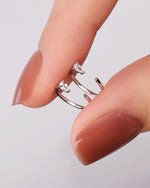 Close-up of silver-tone Meissa Pear Sparkle Huggie Hoop Earrings with clear pear-cut stones held between fingers.