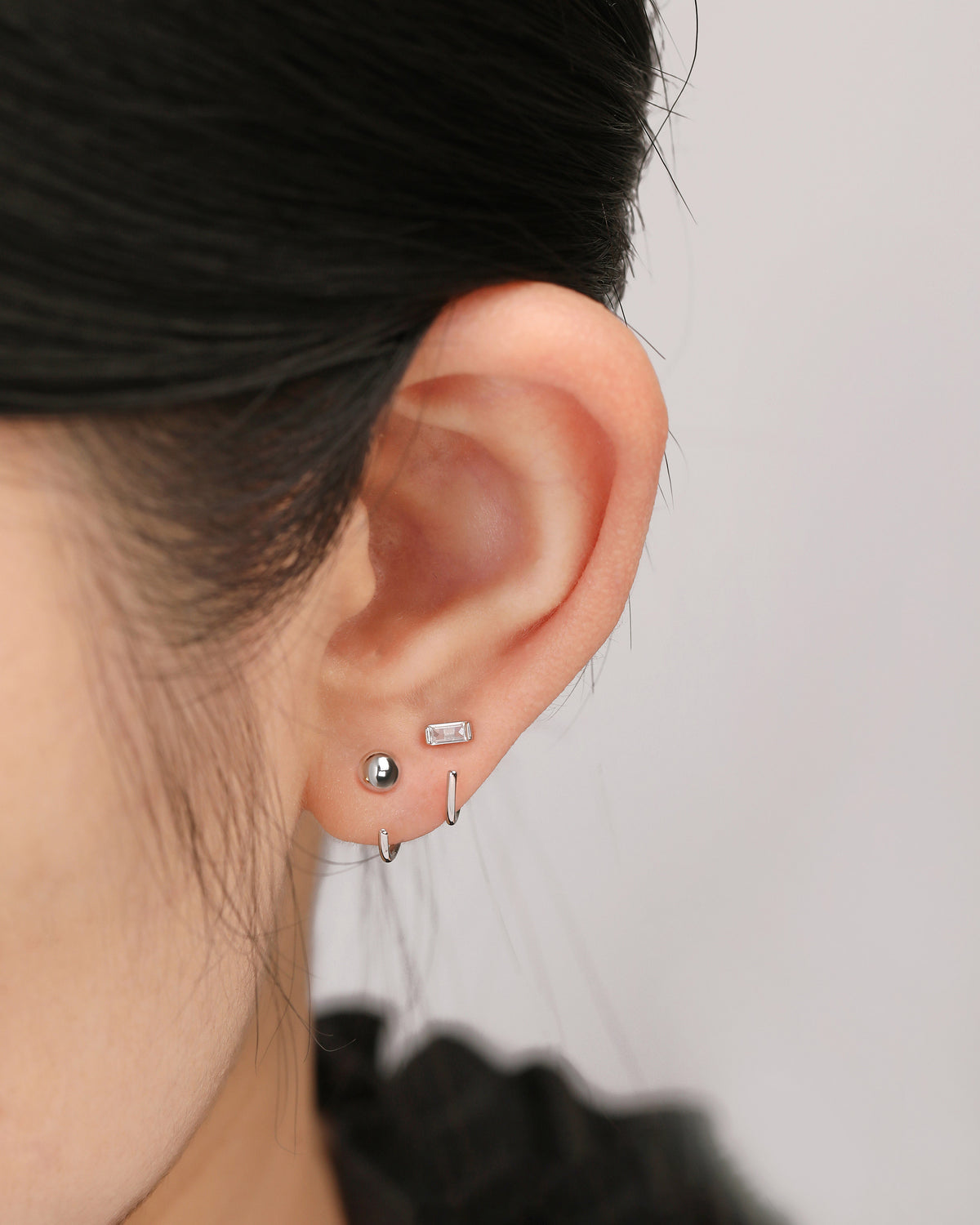 Model wearing silver-tone Meissa Baguette Sparkle Huggie Hoop Earring with ball open hoop earring in a stacked ear look.