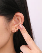 Model wearing gold-tone Meissa Sparkling Bar Huggie Hoop Earring with clear stones and a ball huggie hoop earring in a stacked ear look.