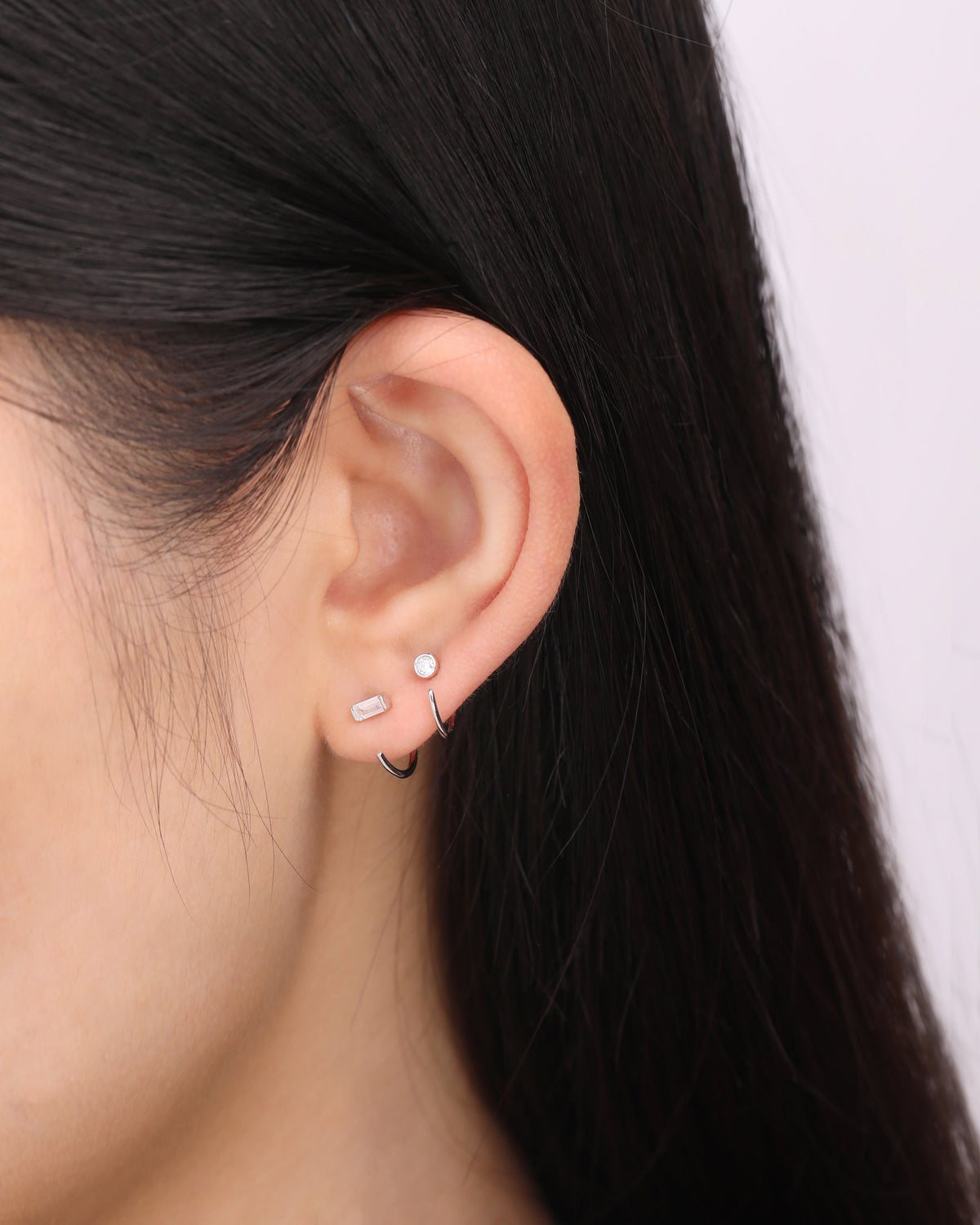 Model wearing a silver-tone Meissa Baguette Sparkle Huggie Hoop Earring and a round sparkle huggie hoop earring in a minimalist stacked ear look.
