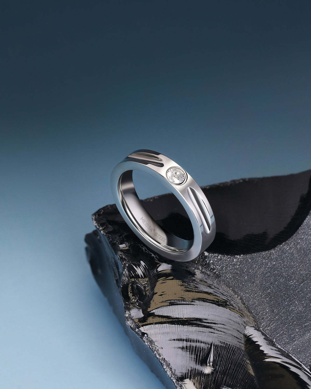 Silver Nova Track Ring in stainless steel displayed on black stone with a blue background, showing the polished band and cubic zirconia center stone.