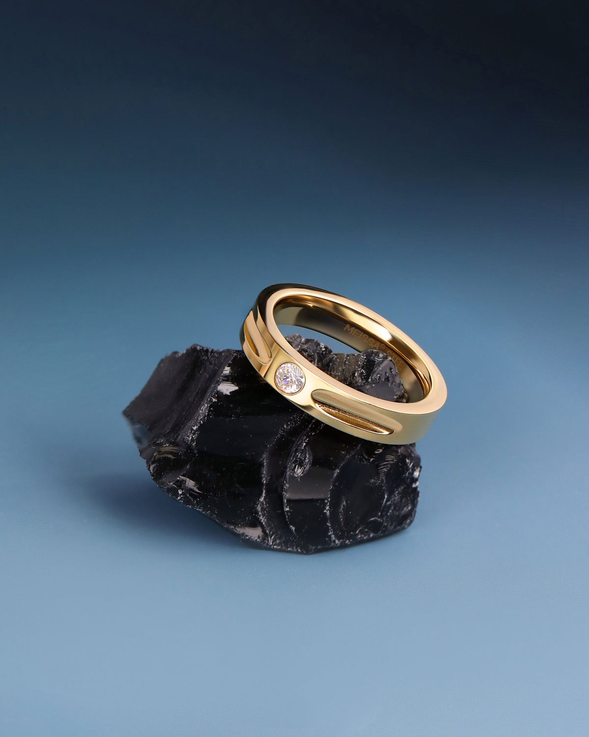 Gold Nova Track Ring in stainless steel displayed on black stone, featuring a round cubic zirconia center stone and polished groove design.