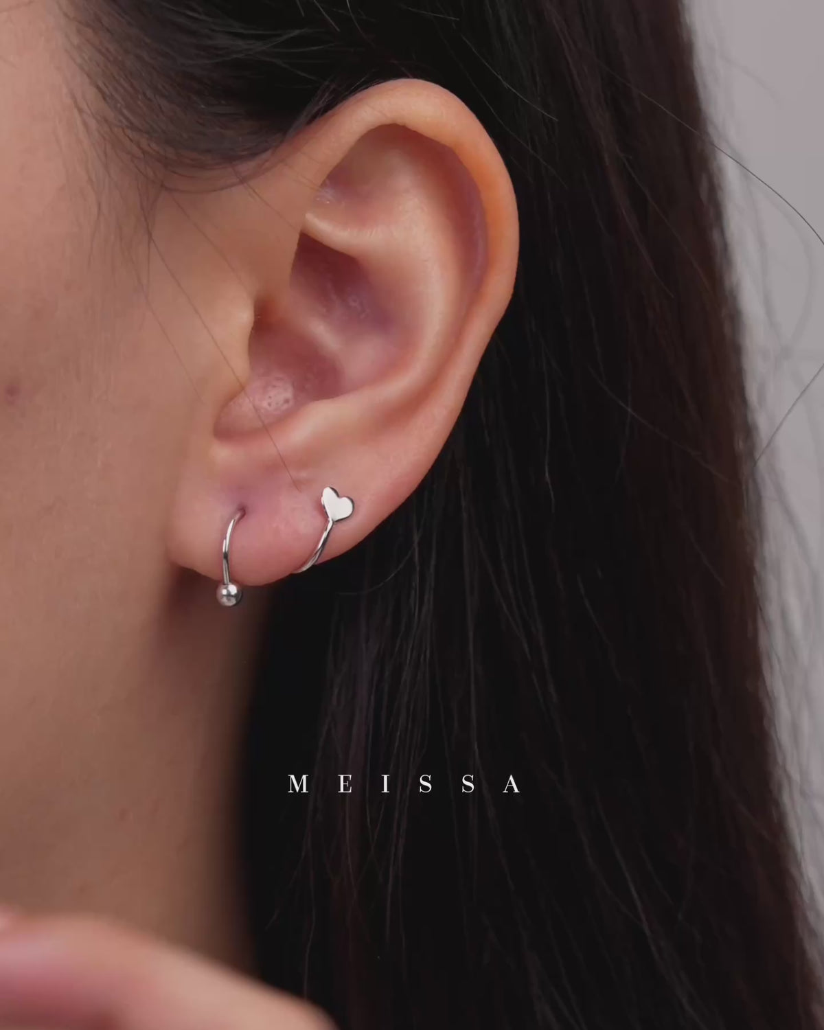 Heart Spiral Screw Back Earrings shown in a close-up video on the ear, highlighting the curved spiral design with a polished heart detail and round screw back ball, while demonstrating how the earring is inserted through the piercing and secured by twisting the ball onto the threaded post.